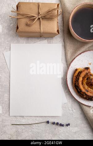Weißes Papier Einladungskarte, Mockup mit Lavendel, Brötchen, Tasse Kaffee, Leinentextilien, Box auf grauem Beton Hintergrund. Blank, flach liegend, Draufsicht, stil Stockfoto