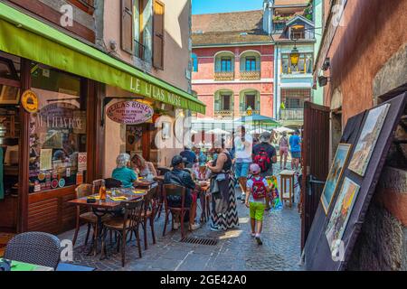Touristen schlendern durch die alten Straßen der Altstadt von Annecy. Souvenirbars und Cafés im Freien ziehen Touristen an. Annecy, Frankreich Stockfoto