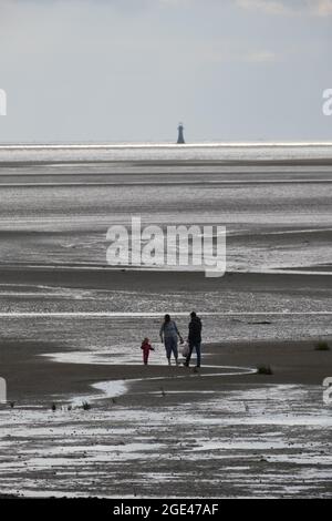 Llanelli, Carmarthenshire, Großbritannien. August 2021. UK Wetter: Sonnige Zauber, aber eine kühle Brise am Llanelli Beach, Carmarthenshire. Eine Familie erkundet den Sand bei Ebbe, während der verdarb stehende Whitford Leuchtturm den Horizont dominiert. Kredit: Gareth Llewelyn/ Alamy Live Nachrichten Stockfoto