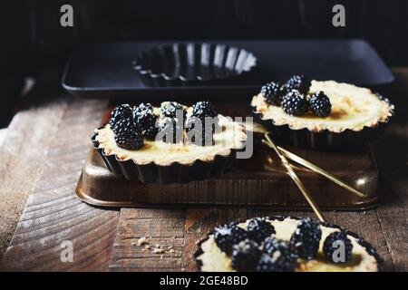 Frisch gebackene Minitörtchen mit Brombeeren auf einem Holztisch. Stockfoto
