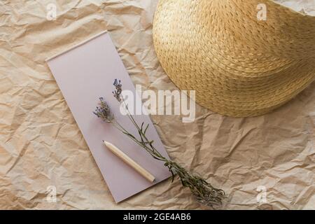 Flache Lay-Komposition mit einem Tränenkraftpapier-Notizblock, Bleistift, getrocknetem Lavendel und Strohhut auf einem Kraftpapier-Hintergrund. Draufsicht. Stockfoto