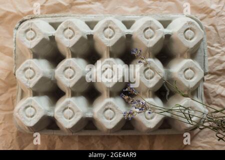 Isolierter geschlossener Eierkarton mit getrockneten Lavendelfeldern auf zerknittertem Kraftpapier-Hintergrund. Bio-Eierkarton oder Eierbehälter Draufsicht. Stockfoto