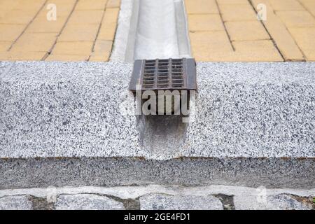 Drainage Rost-System, Grill für die Entfernung von Regenwasser aus Stein Gehwege durch Graben und Loch in Granit Curbe auf der Straße schließen, niemand. Stockfoto