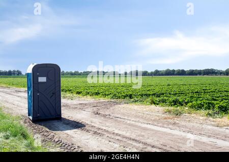 Öffentliche Kunststoff tragbare Toilette auf dem landwirtschaftlichen Feld der Farmerlandschaft mit blauem Himmel, im Freien Stockfoto