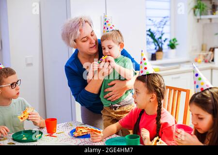 Unterstützende Mutter hilft kleinen Jungen, Party-Horn zu blasen Stockfoto