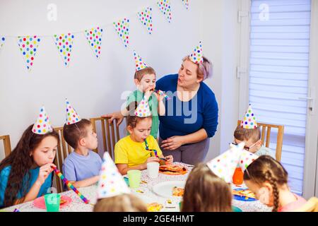 Unterstützende Mutter hilft kleinen Jungen, Party-Horn zu blasen Stockfoto