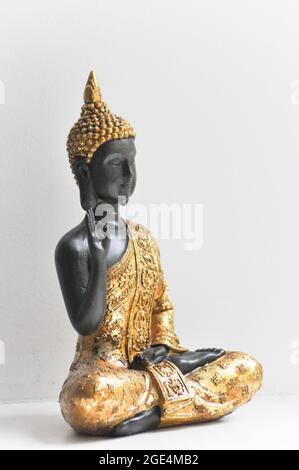 Eine goldene Buddha-Statue, die in der Mitte des Bildes vor einem weißen Hintergrund aufgestellt ist. Stockfoto