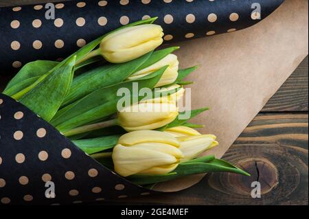 Gelbe Tulpen in polka dot Kraftumschlag auf dunkel verwitterten Holztisch. Platz für Text Stockfoto