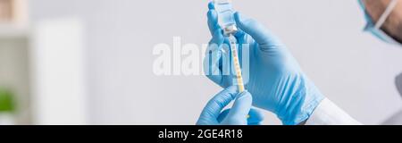 Teilansicht des Arztes in blauen Latexhandschuhen, die eine Spritze mit Coronavirus-Impfstoff füllen, Banner Stockfoto