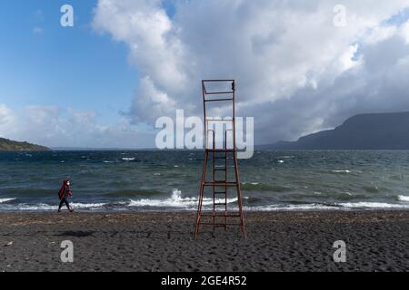 Pucon, Araukanien, Chile. August 2021. Eine Frau mit Gesichtsbehang spaziert am Montagmorgen vor dem Sturm am Ufer des Lago Villarrica in Pucon im Süden Chiles entlang. Für diese Woche wird von der Hauptstadt Santiago im Süden schlechtes Wetter erwartet, bei dem es der wichtigste Regen des Jahres für die südzentrale Zone Chiles sein könnte. (Bild: © Matias Basualdo/ZUMA Press Wire) Bild: ZUMA Press, Inc./Alamy Live News Stockfoto