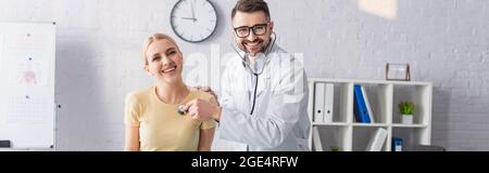 Glücklicher Arzt und Patient beim Blick auf die Kamera während der Diagnose in der Klinik, Banner Stockfoto