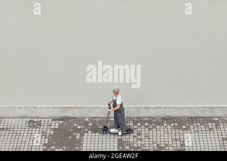 Grafische Weitwinkelansicht auf zeitgenössische reife Frau Reiten Elektroroller in der Stadt über gekachelten Hintergrund, kopieren Raum Stockfoto