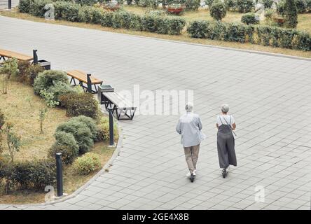 Weitwinkel-Rückansicht auf moderne ältere Paar Reiten Elektroroller im Park, Platz kopieren Stockfoto