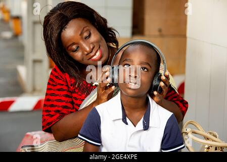 Reife Frau, die im Freien sitzt und den Helm ihres Kindes anpasst, während sie lächelt. Stockfoto