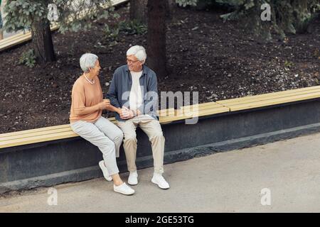 Porträt eines modernen älteren Ehepaares, das auf einer Bank im Park sitzt, während er ein romantisches Date genießt und Platz kopiert Stockfoto