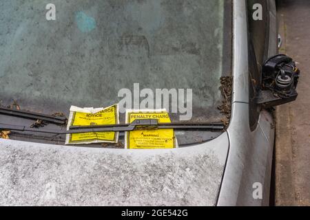 Verlassene Autos mit zwei Entgeltanzeigen an einer schmutzigen Windschutzscheibe, England, Großbritannien Stockfoto