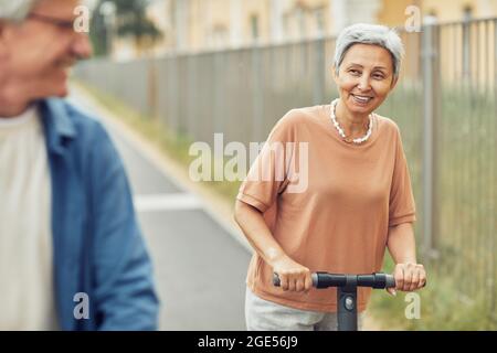 Porträt eines modernen älteren Ehepaares, das im Freien in einer wunderschönen Stadt mit Elektrorollern unterwegs ist, Platz zum Kopieren Stockfoto