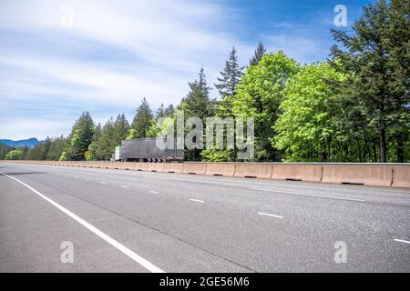 Industrieller langer Schlepper großer grüner Sattelschlepper, der kommerzielle Ladung in geteerten trockenen Transporter transportiert, der auf der kurvenreichen Autobahn ro läuft Stockfoto