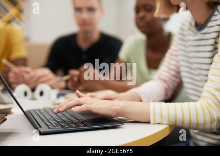 Seitenansicht Nahaufnahme einer Gruppe junger Menschen, die zusammen am Tisch in der Universitätsbibliothek studieren, Fokus auf weibliche Hände, die auf der Laptop-Tastatur tippen, Kopierraum Stockfoto