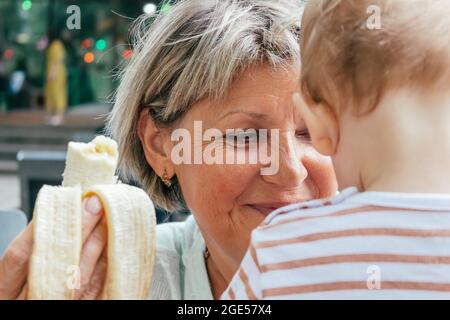 Oma lächelt, füttert ihren Enkel mit Baby-Banane. Stockfoto