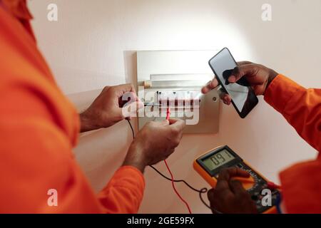 Hände von Technikern, die Multimeter verwenden, um elektrischen Strom in Watt-Betriebsstundenzähler zu testen Stockfoto
