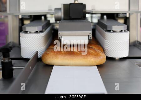 Brote, die auf einem Förderband aus Weizenmehl zubereitet werden. Automatisierte Bäckerei Produktionslinie. Selektiver Fokus. Stockfoto