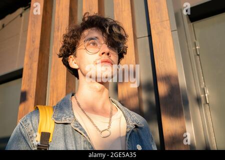 Gelassener junger Mann in Denim-Jacke und T-Shirt, der an sonnigen Tagen im Freien steht Stockfoto