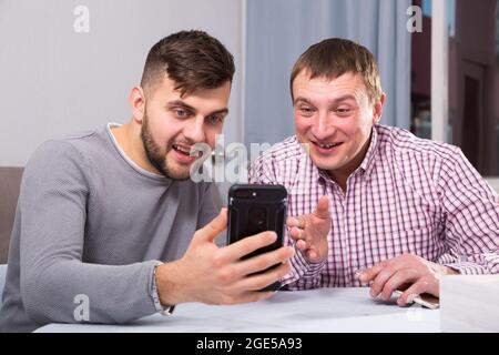 Fröhliche Männer, die zu Hause telefonieren Stockfoto