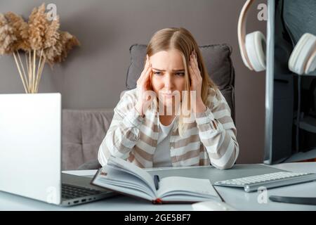 Junge Frau in Stress machen Büroarbeit über pc-Laptop. Müde junge Frau mit Kopfschmerzen aufgrund der Frist Überstunden Problem. Der Student leidet unter E-Learning Stockfoto