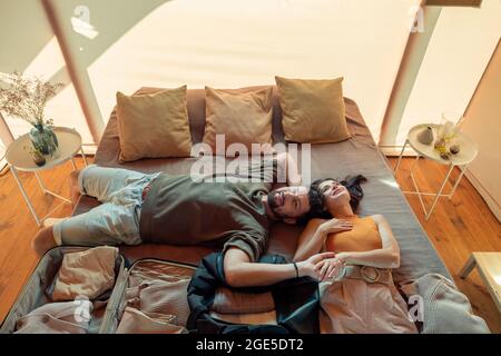 Glückliches Paar, das mit ausgepacktem Gepäck auf dem Bett lag und träumte Stockfoto