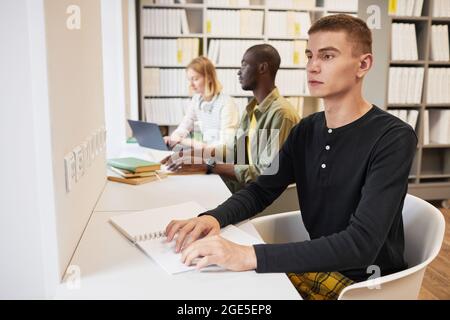 Seitenansicht einer Gruppe von Studenten mit einem jungen Mann, der in der Bibliothek Brailleschrift liest Stockfoto