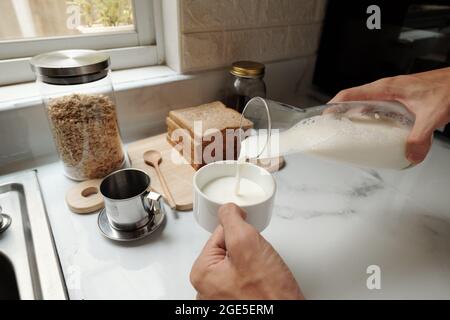Menschenhände, die morgens beim Frühstück Milch in eine Tasse Kaffee gießen Stockfoto