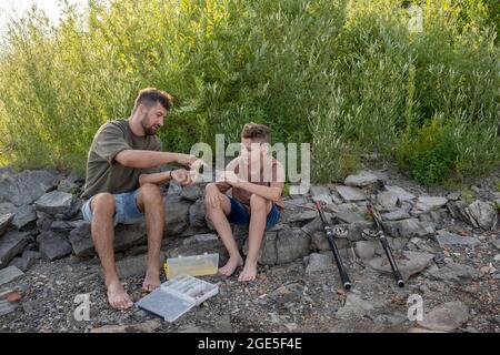 Junger Mann, der seinem Sohn im Teenageralter zeigt, wie man Fischköder wählt und zubereitet Stockfoto