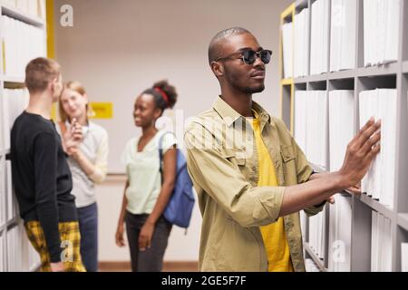 Porträt eines blinden afroamerikanischen Mannes, der Buch in der Bibliothek auswählt Stockfoto