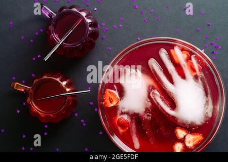 Happy Halloween Party flach Lay Komposition. Schüssel mit blutigem Farbgetränk, gefrorenen Händen, Cocktailgläsern auf schwarzem Hintergrund. Draufsicht, Overhead. Stockfoto