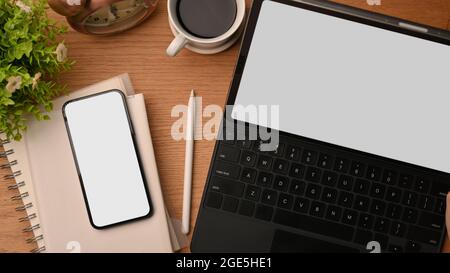 Femininer, gemütlicher Arbeitsplatz mit weißem Tablet-PC-Modell, magischer Tastatur, Smartphone-Modell mit leerem Bildschirm, Notebooks, Kaffee und Dekor auf holzbraunem Ba Stockfoto