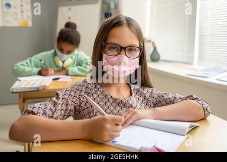 Zeitgenössische schulmädchen in Maske und Brille Blick auf Sie in der Lektion Stockfoto