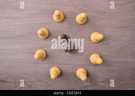 Social Mobbing-Konzept mit weißen Schachfiguren, die einen Kreis bilden und in der Mitte ein schwarzes Stück auf dem Boden liegen lassen Stockfoto