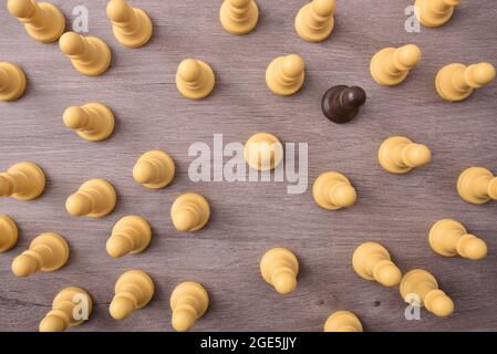 Konzept der sozialen Unterschiede mit schwarzem Schachspiel, umgeben von weißen Stücken auf einem Holztisch. Draufsicht. Stockfoto