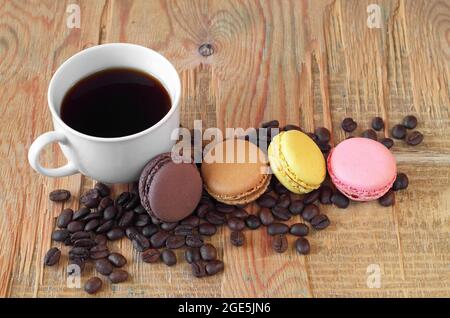Kaffeetasse, Bohnen und kleine französische Makronen auf altem Holzhintergrund Stockfoto