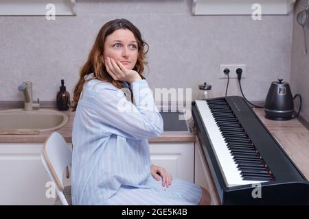 Probleme beim Lernen, ein Musikinstrument zu Hause zu spielen. Frau traurig darüber, dass sie alleine Musik auf einem Synthesizer spielen lernt Stockfoto