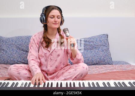 Eine Musikerin sang ins Mikrofon und spielte Klavier auf dem Heimbett im Schlafzimmer Stockfoto