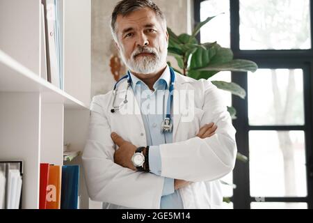 Porträt eines gut aussehenden, reifen Arztes, der im modernen Büro am Fenster steht. Stockfoto