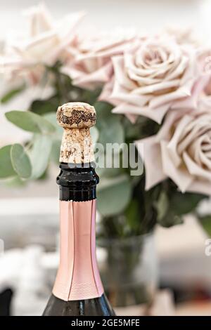 Nahaufnahme offene Flasche mit alkoholischem Getränk und einem Strauß Rosen im Hintergrund. Champagner oder Sekt. Konzept für Veranstaltungen oder Feiern. Kopie sp Stockfoto