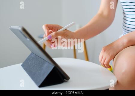Nahaufnahme einer Frau, die auf dem Tablet skizziert oder zeichnet, mit einem Eingabestift im komfortablen weißen Wohnzimmer. Web-Designer oder Freiberufler Konzept Stockfoto