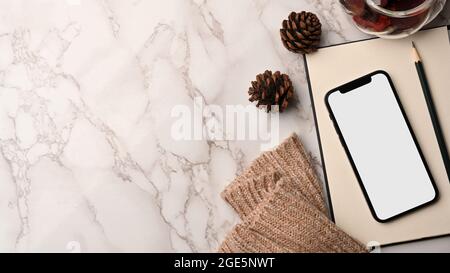 Herbstzusammensetzung Eckrand, Arbeitsplatz mit Kopierraum auf Marmorhintergrund, Smartphone leerer Bildschirm Mockup, Notizbuch, Kiefernzapfen, gestricktes Sweat Stockfoto
