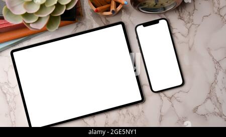 Zwei Geräte in flachem Layout, Smart Tablet und Smartphone-Modell, leerer Bildschirm für Ihre Marken, auf Marmorhintergrund, Arbeitsplatzdekorationen Stockfoto