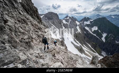 Wanderer und Frauen steigen in felsiges Gelände, Bergpanorama mit felsigen Gipfeln im Hintergrund, dramatischer Wolkenhimmel, Heilbronner Weg, Allgäu Alpen Stockfoto