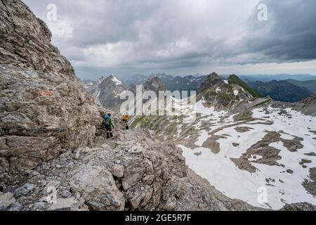 Wanderer und Wanderer bergab felsiges Gelände, im Hintergrund Bergpanorama mit alten Schneefeldern und felsigen Berggipfeln, Heilbronner Weg, Allgäu Stockfoto