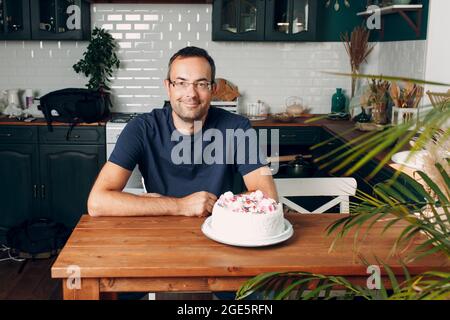 Mann sitzt in der heimischen Küche mit Kuchen auf dem Tisch. Stockfoto